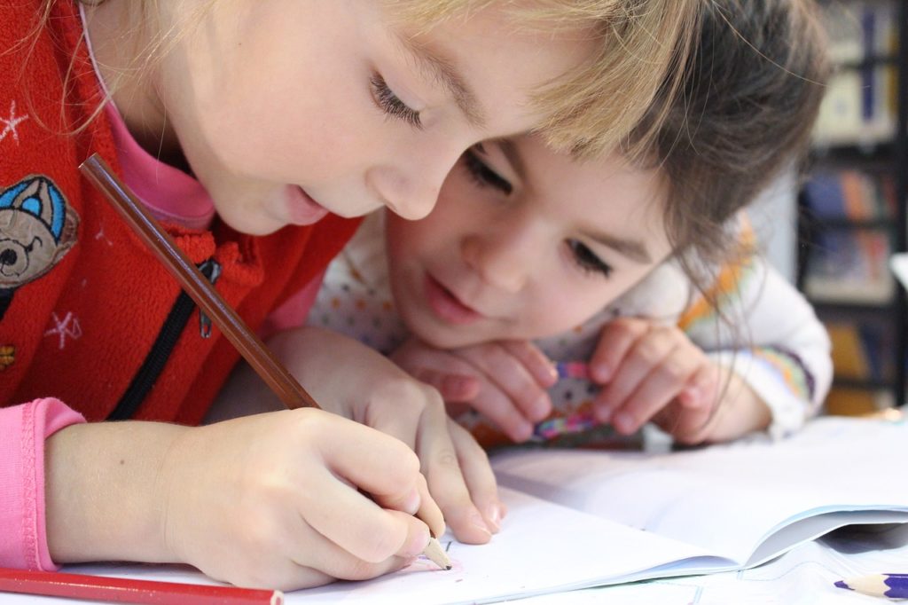 two young children writing in a book together