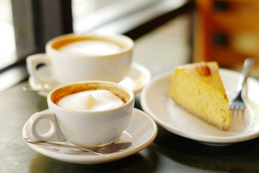 Two cups of coffee and a slice of cake on a table.