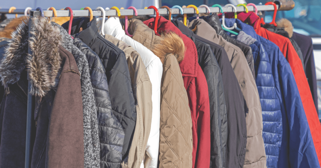 A row of winter jackets, including brown, white, red, and blue colours, hanging on a metal rack outdoors.