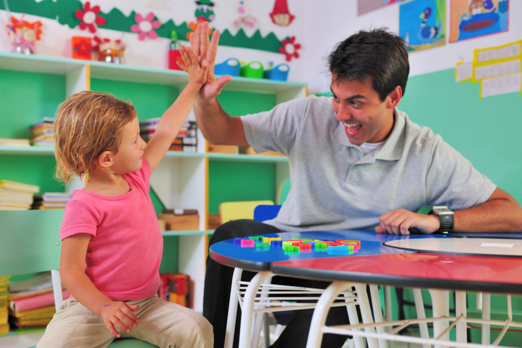 A child and preschool teacher high-fiving each other in a classroom.