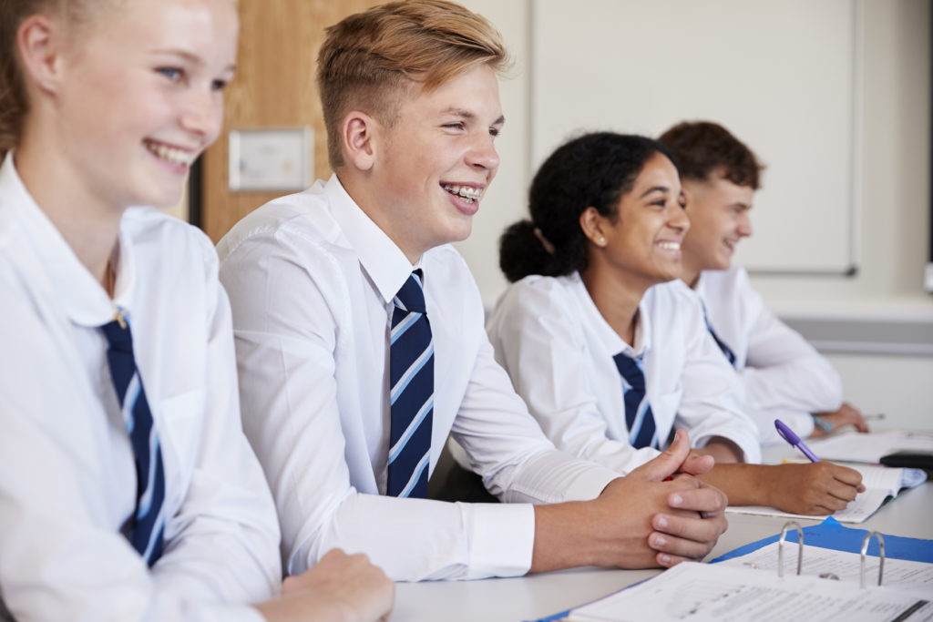 Line of secondary school students wearing uniforms sitting at their desks in a classroom.