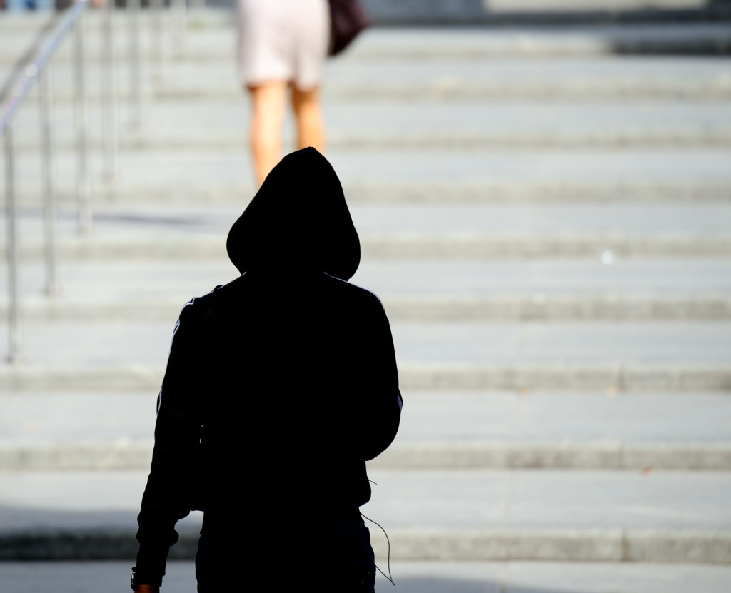 A woman being followed up a row of steps by a hooded figure.