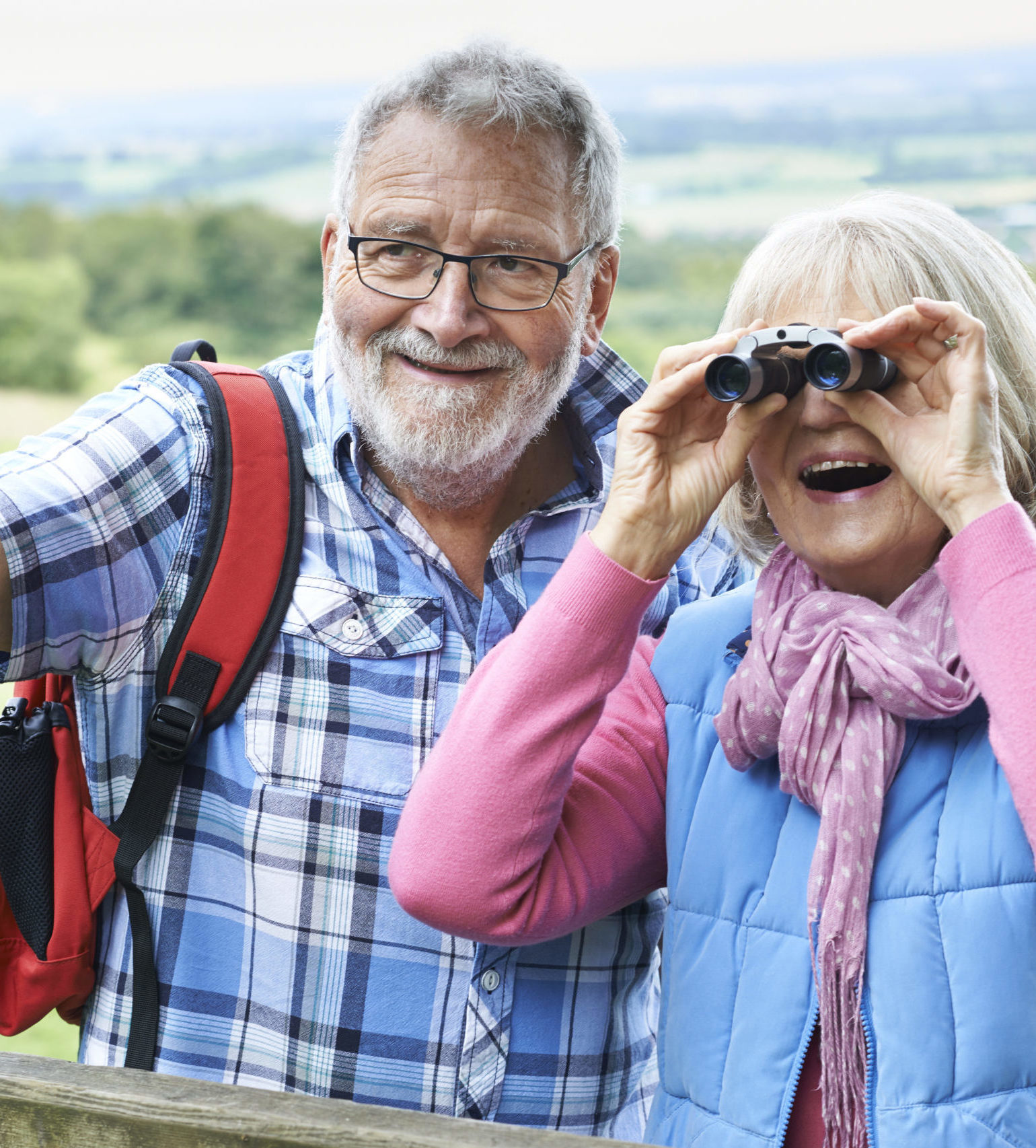Senior Couple Hiking In Countryside Looking Through Binoculars
