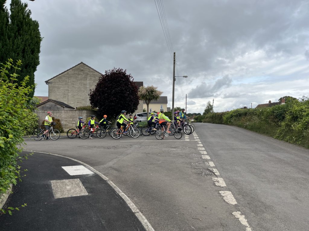 Bikeability instructors with a class of children riding bicycles, stopped at a junction.