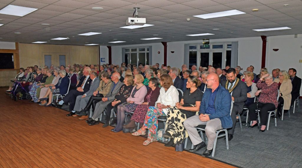 award winners wait to receive their certificates, seated in the hall