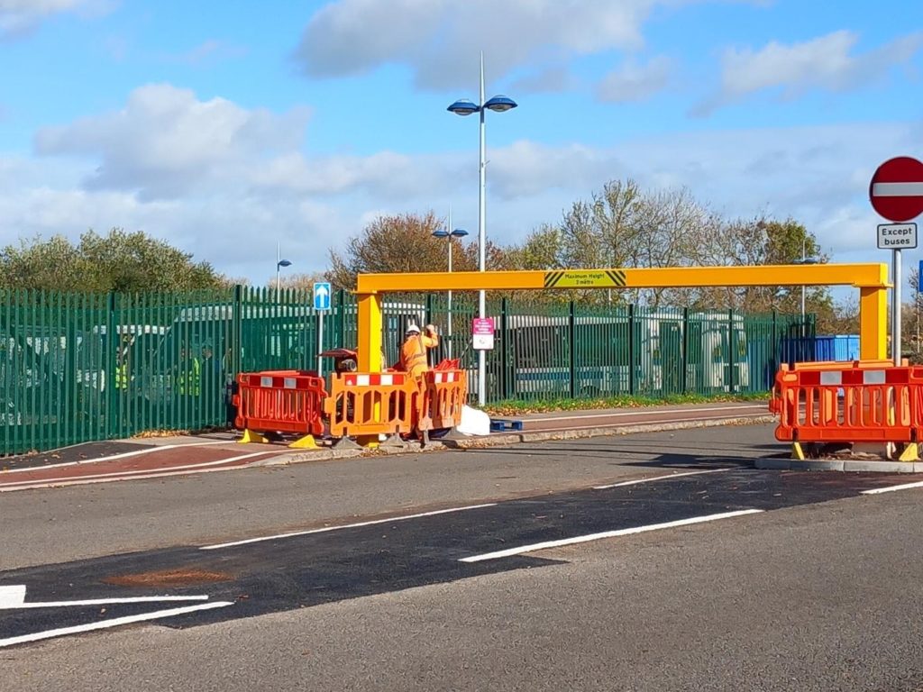 Construction workers installing height restriction barriers at Silk Mills Park and Ride on a clear, sunny day.