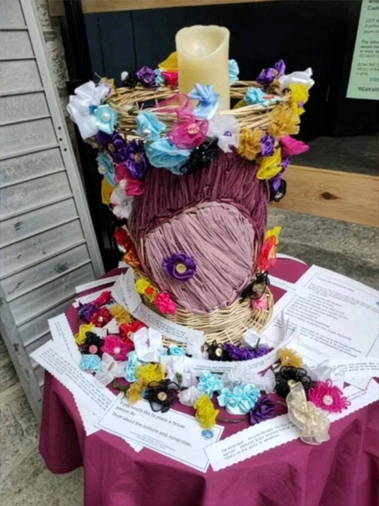 Decorative Holocaust Memorial candle surrounded by colourful handmade flowers and remembrance messages on display at Taunton Library.
