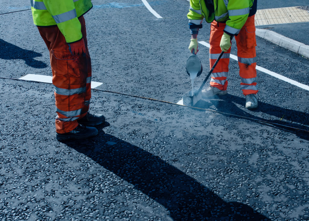 Roadworker applying thermoplastic road marking on the freshly laid tarmac during new roundabout and access road construction.