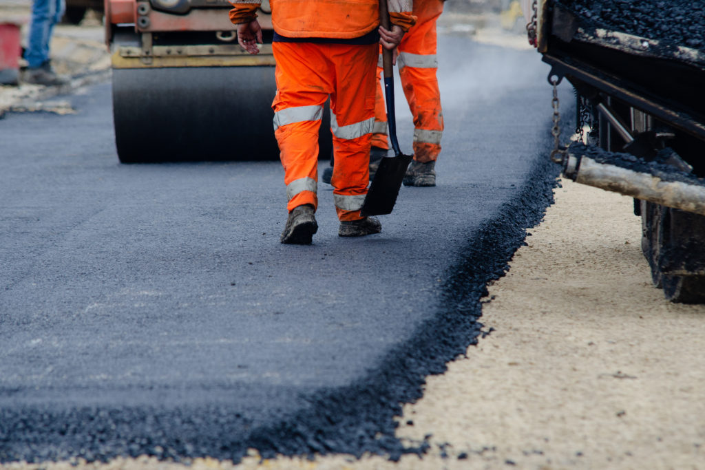 Roadworkers placing hot tarmac during a new road construction project, with workers in high-vis clothing resurfacing a road.