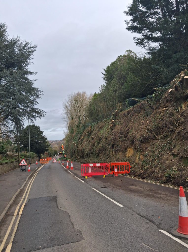A30 Hendford Hill, Yeovil, after Storm Chandra, showing lane closure with cones and barriers beside a damaged roadside embankment.