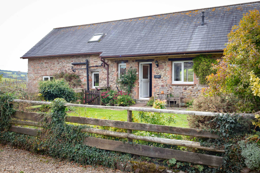 Stone cottage with a small garden, wooden fence, and outdoor seating, set in a rural setting.