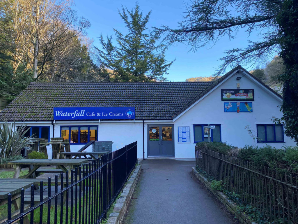 Exterior of Waterfall Cafe and Ice Creams building with outdoor benches and signage on a paved path.