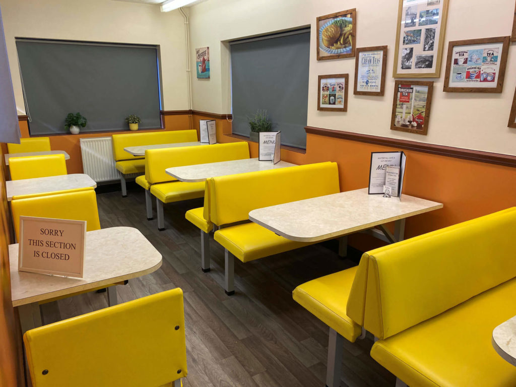 Cafe interior with yellow booth seating, tables with menus, and a sign indicating a closed section.