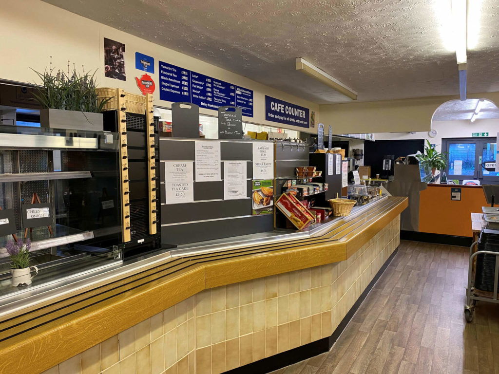 Cafe counter with menu boards overhead, drinks display, and food service area with equipment and supplies.
