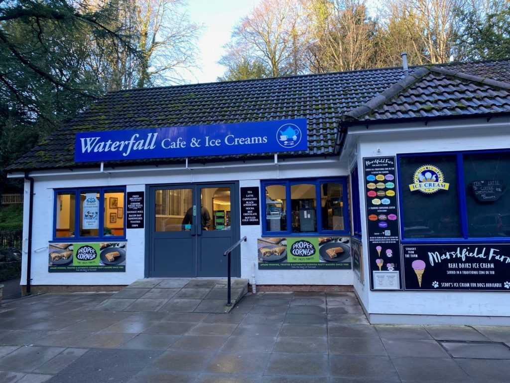 Exterior of Waterfall Cafe and Ice Creams building with outdoor benches and signage on a paved path.
