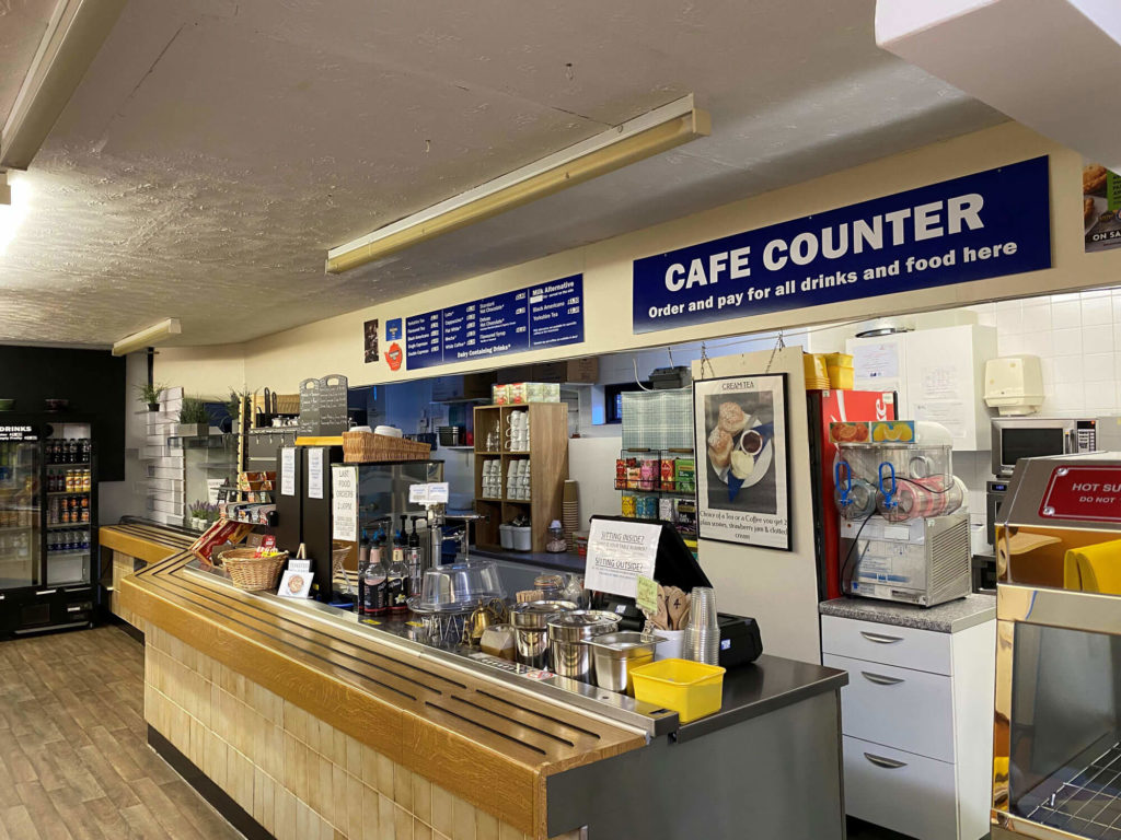 Cafe counter with menu boards overhead, drinks display, and food service area with equipment and supplies.