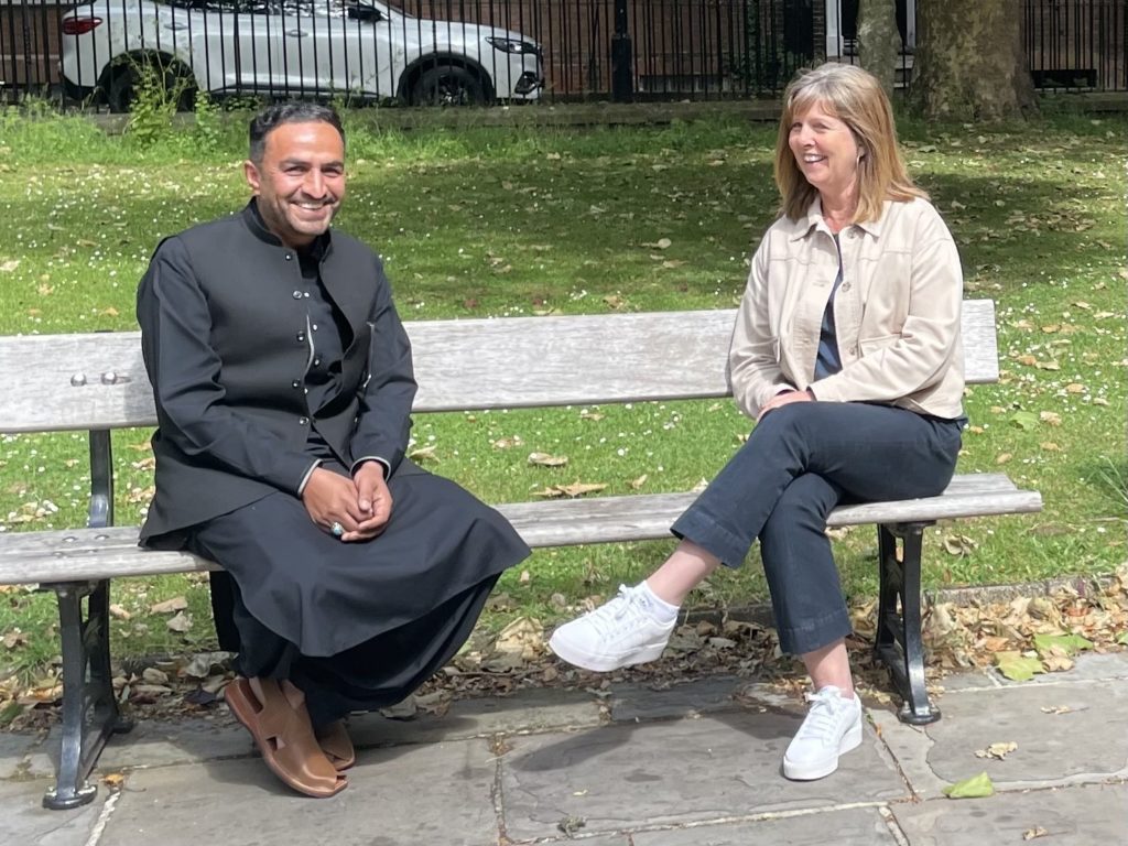 Abdul sits with a Somerset Council Displaced People Service staff member on a park bench during Refugee Week campaign.