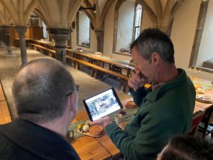 Two men stand in the Undercroft at The Bishops Palace in Wells. The man on the right is holding an iPad and showing the other man, Col Needham, a photo on the screen