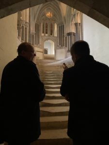 Two men stand at the bottom of a set of ancient steps, talking.