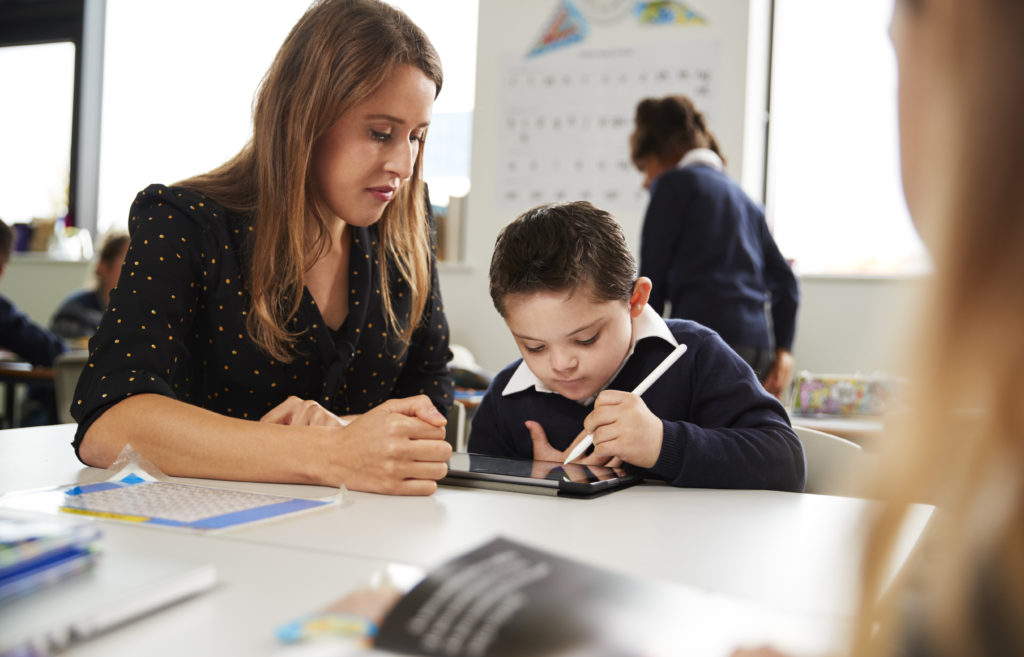 Teacher supports young pupil using a tablet in classroom, illustrating personalised learning and additional education support.