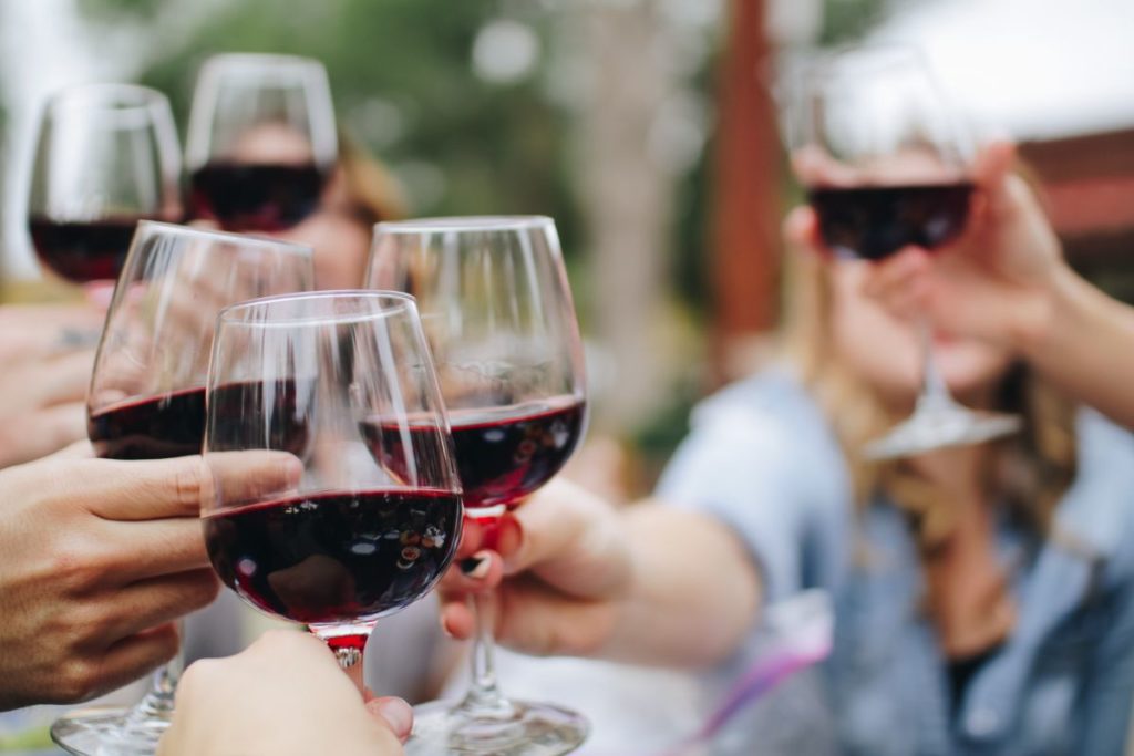 People raising glasses of red wine in a social setting, making a toast together outdoors.