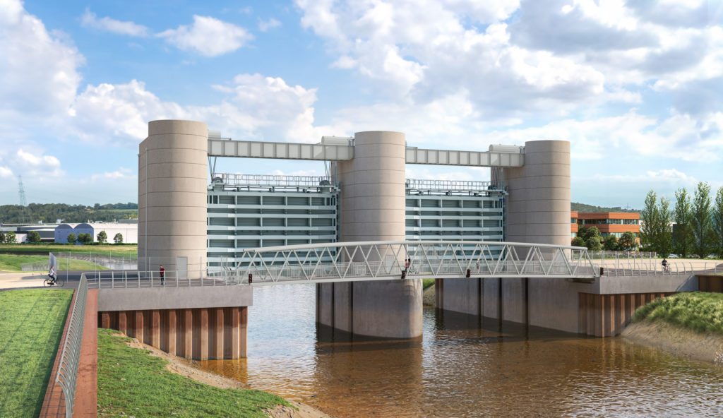 Side view of the tidal barrier across the river. There are 3 large oval concrete pillars, one on each edge and one in the middle of the river, joined by a structure in between. There is a bridge in front of the barrier which pedestrians can use.