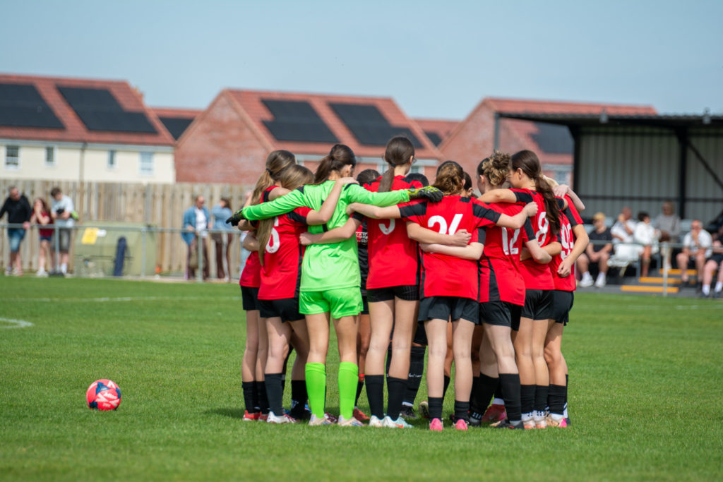 Group of girls on a football pitch in a huddle in a football game by Somerset FA.
