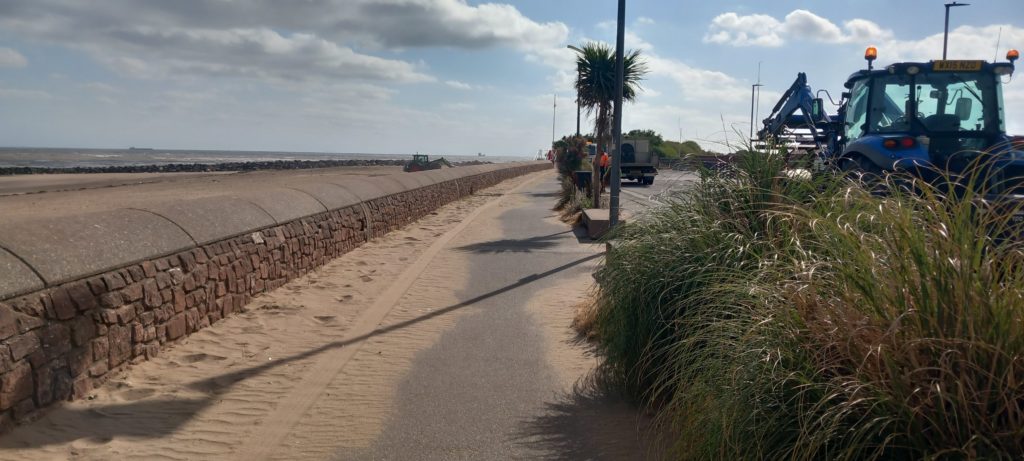 sand on the road below a wall with the sea and beach in the background