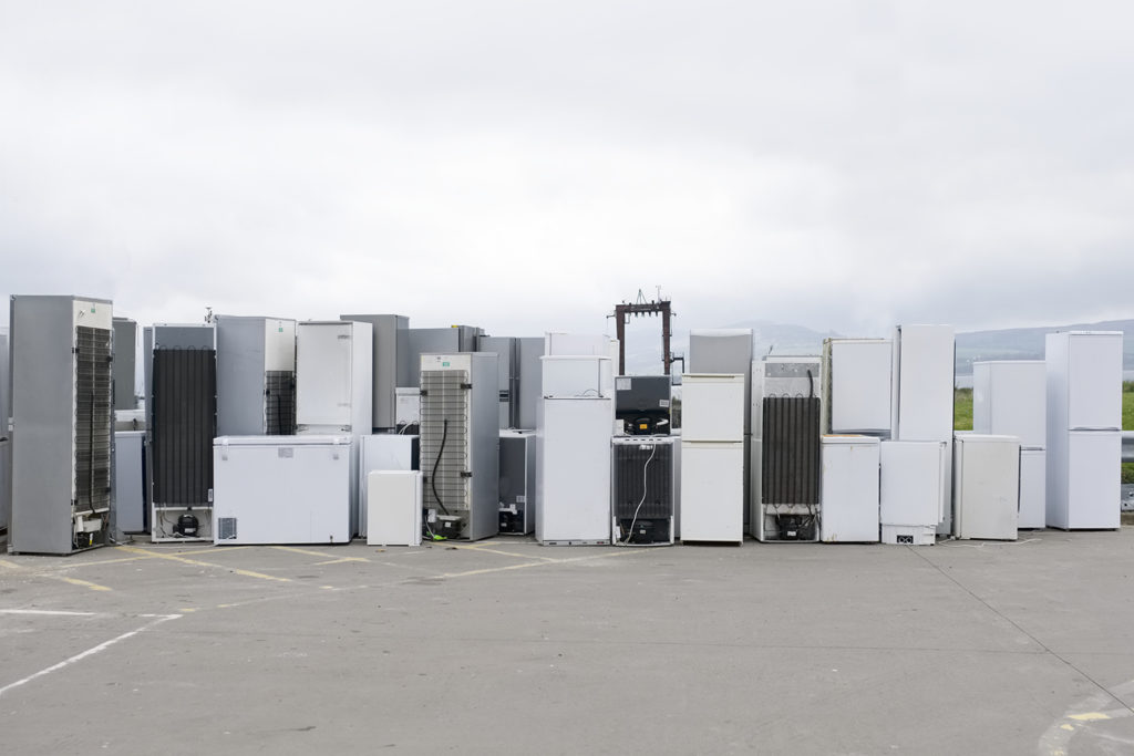 Rows of discarded fridges and freezers stacked at a recycling facility, ready for processing and materials recovery.