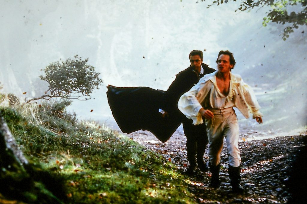 Two men in Georgian clothes walking along a path in a woodland.