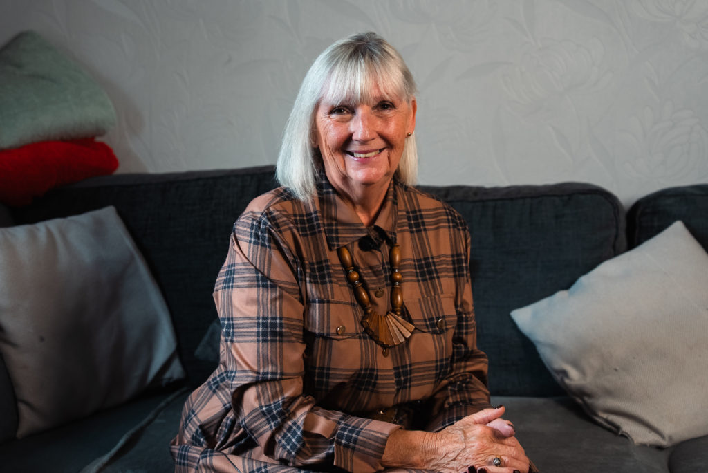 Kinship carer Valerie sits smiling on a sofa at home, sharing her story during Kinship Care Week in Somerset.